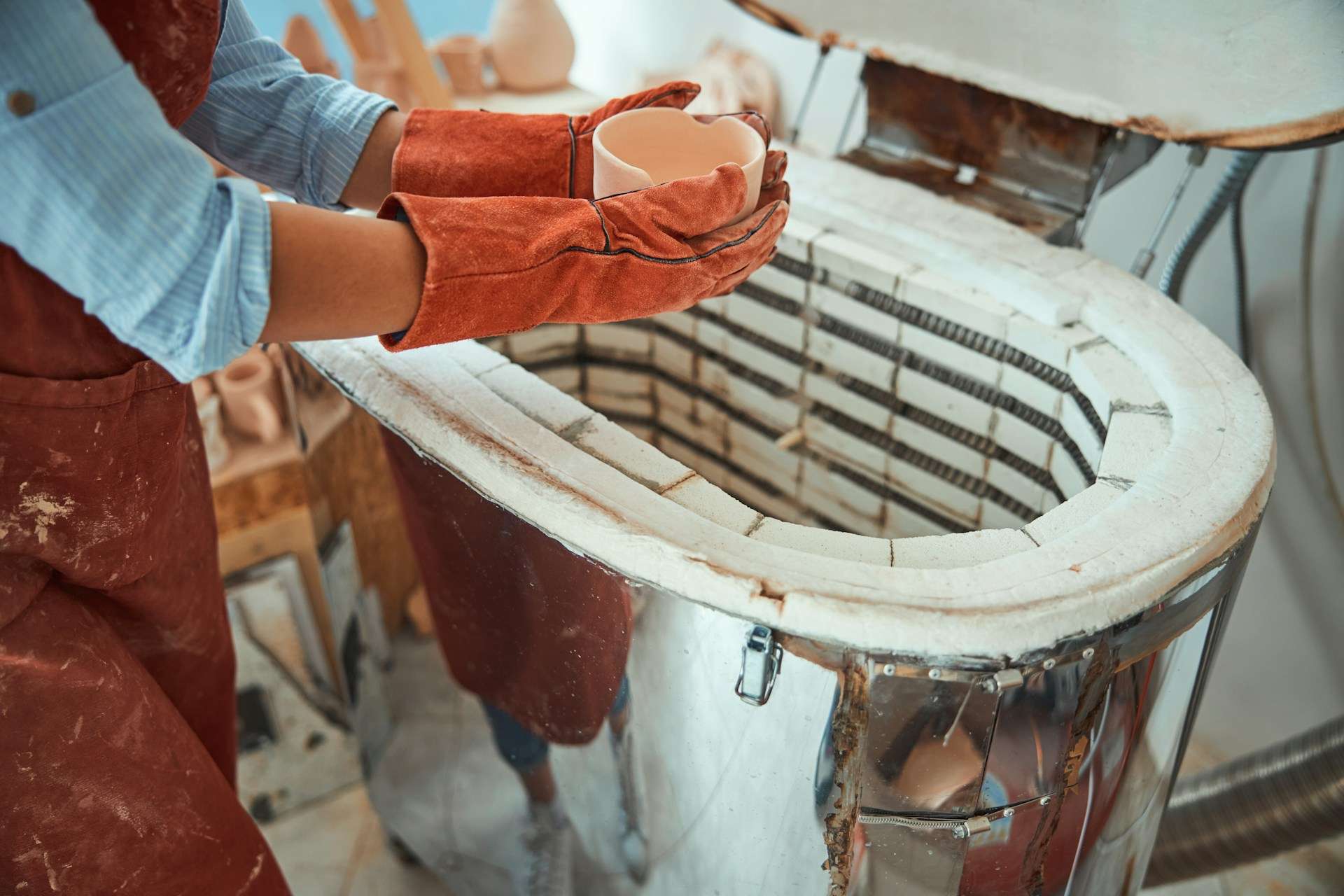 A student wearing protective gloves loads ceramic pieces into a kiln for the firing process.