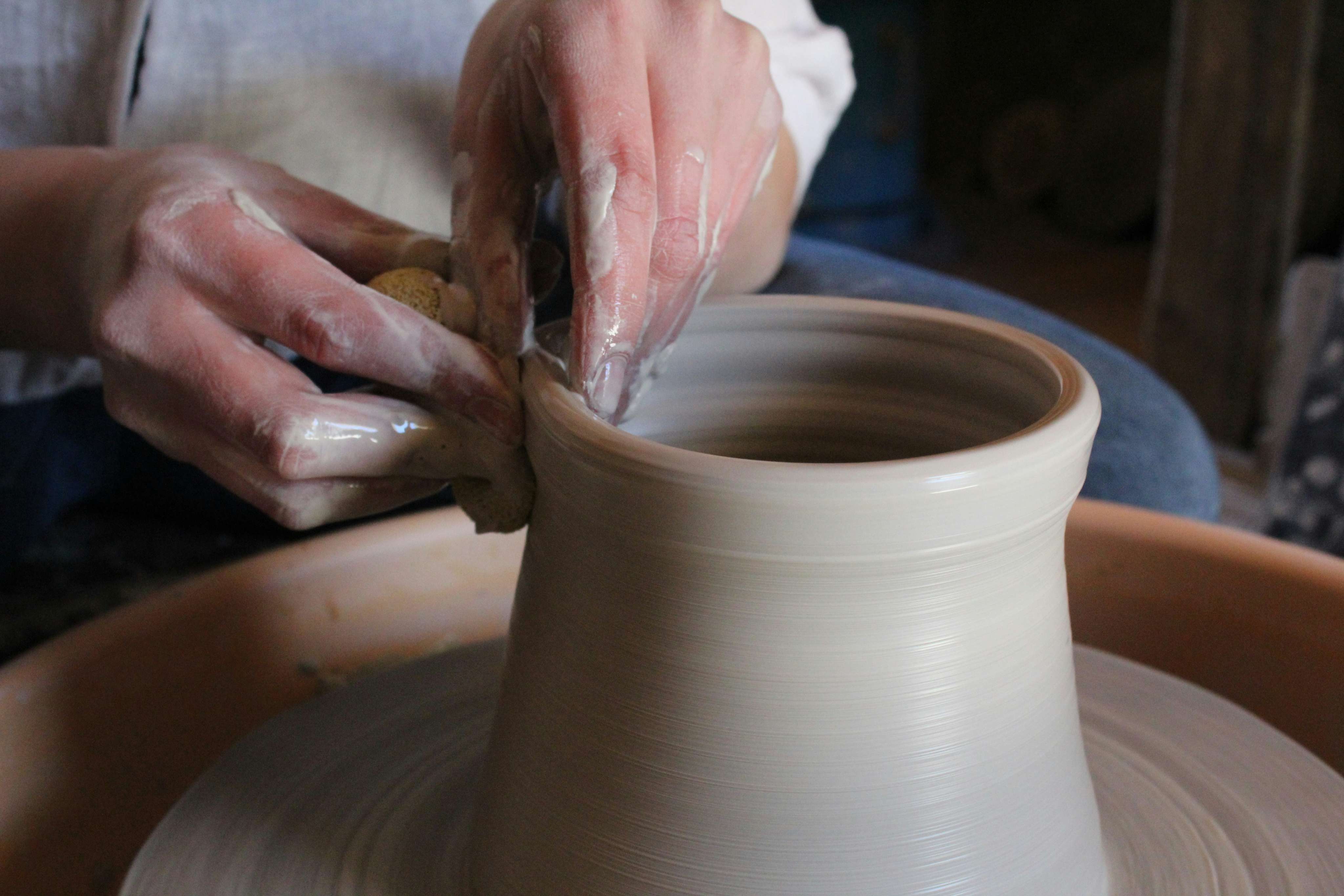 Close-up of hands carefully throwing and shaping a clay vase on a pottery wheel.