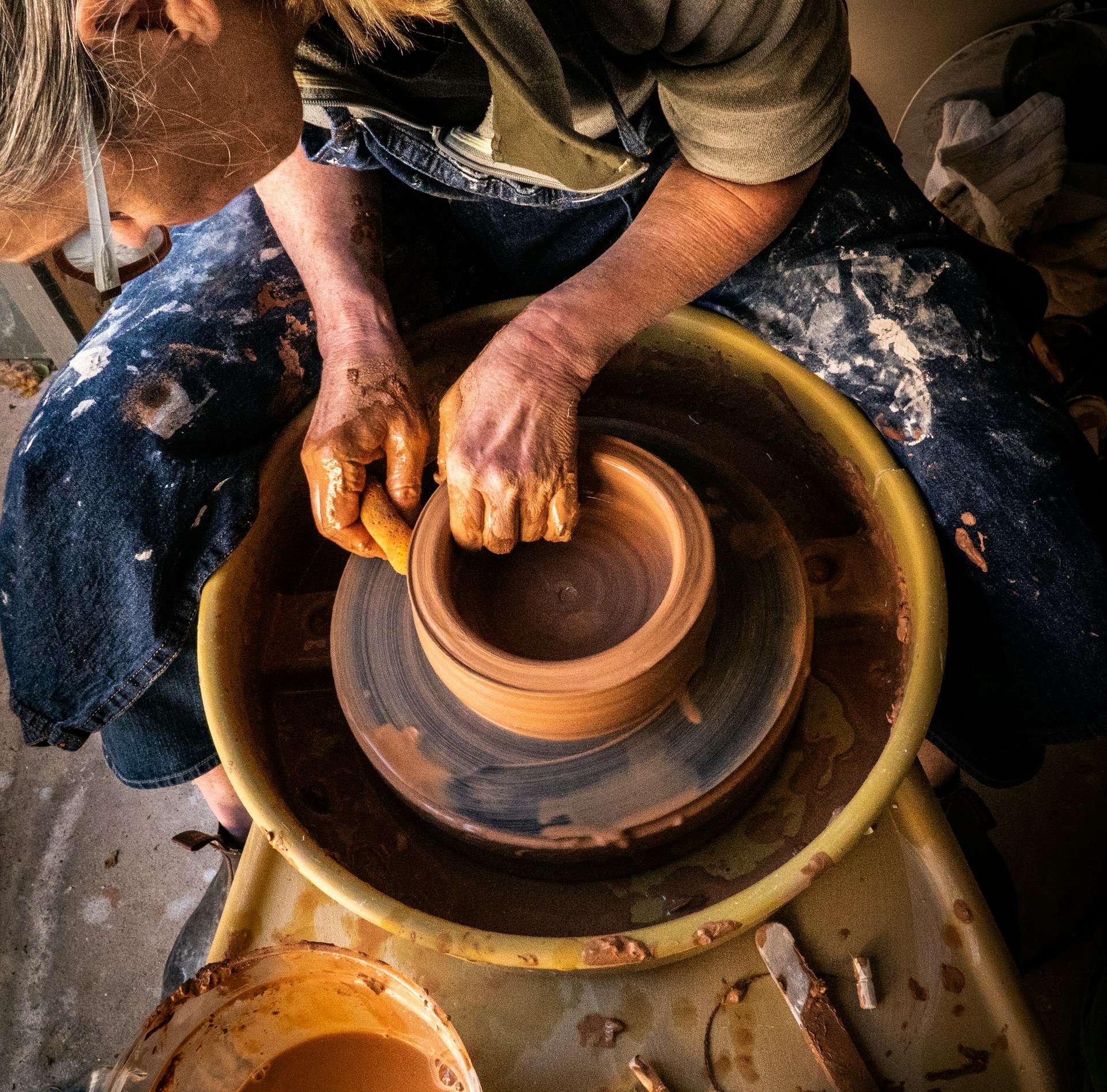 Overhead view of a potter's clay-covered hands centering clay on a wheel during a beginner class at Pinch Pot Ceramics.